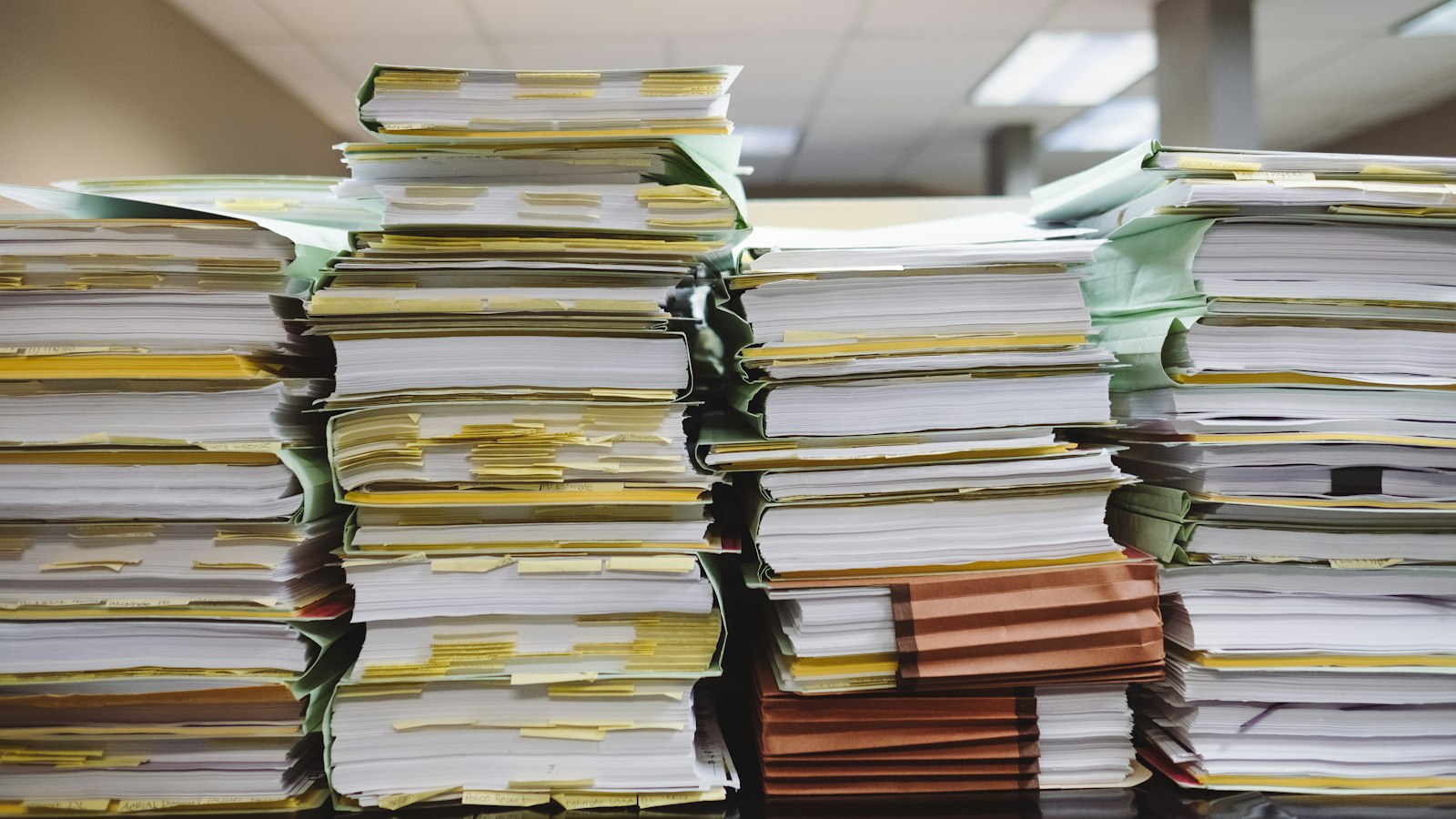 Tall stacks of paper documents and file folders piled on an office desk