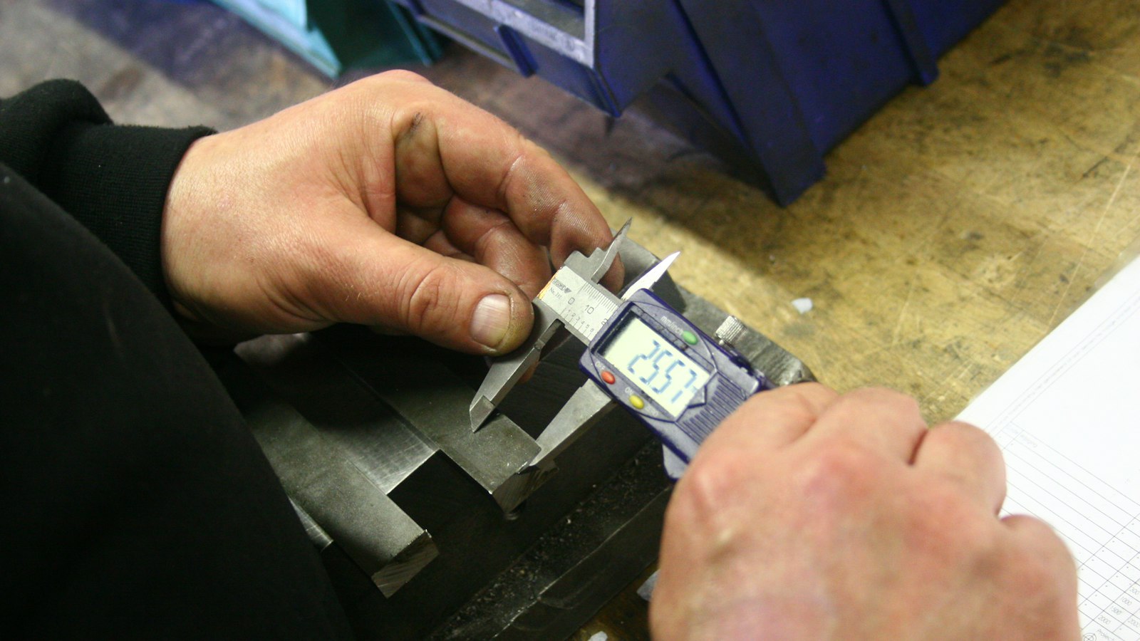 Hands using a digital caliper to measure a metal part on a workbench