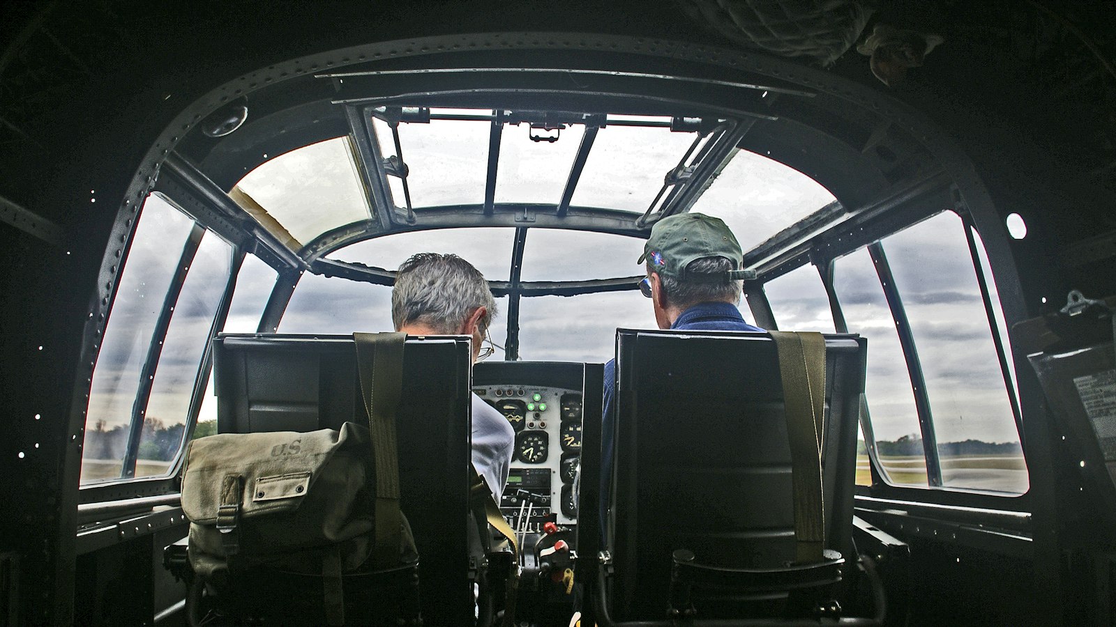 Two pilots seen from behind in the cockpit of a vintage aircraft before takeoff