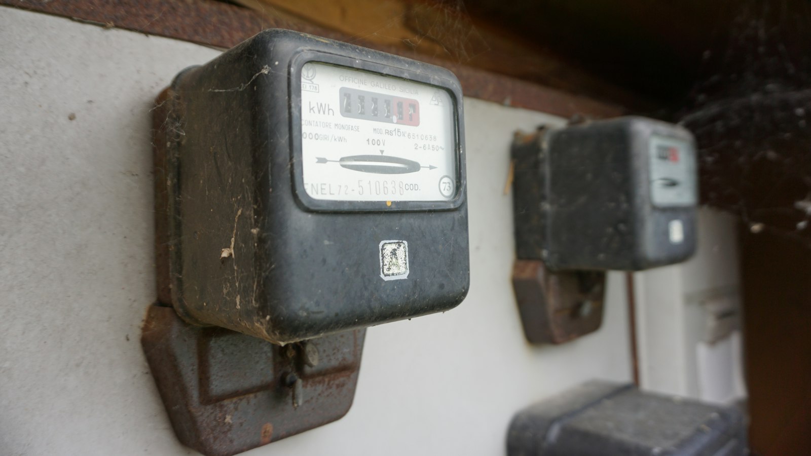 Two old electricity meters mounted on a wall, one showing a kilowatt hour dial