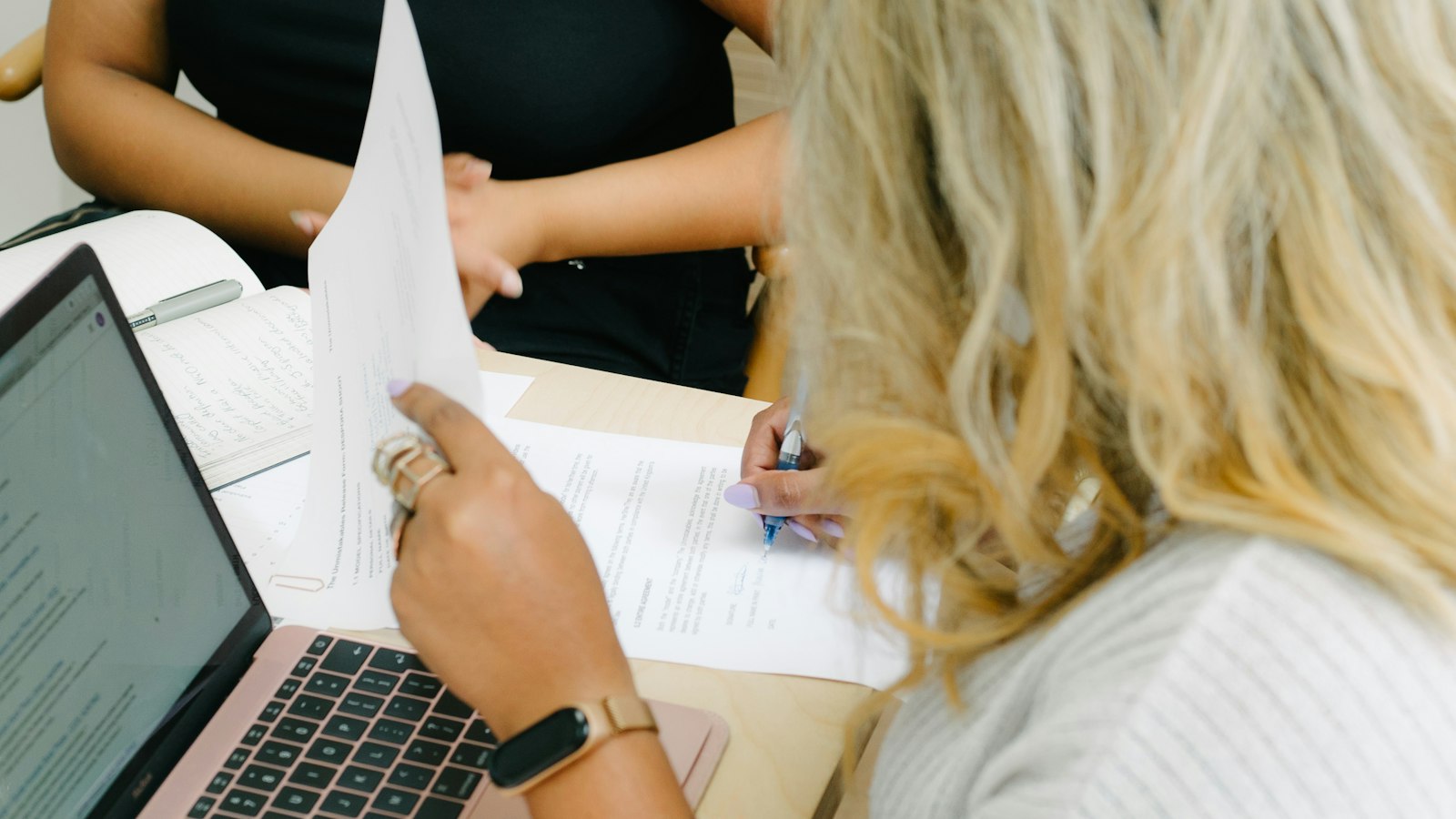 Two people at a table reviewing printed papers beside an open laptop