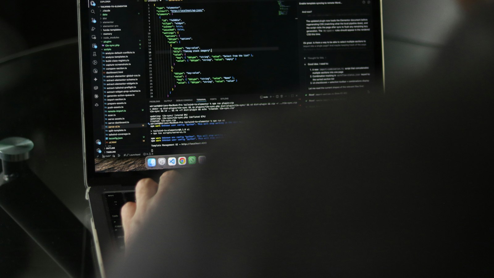 Person typing at a laptop showing lines of code in a dark room
