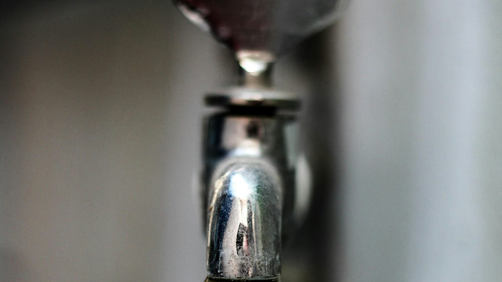 A close up of a chrome faucet with a drop of water forming at the spout